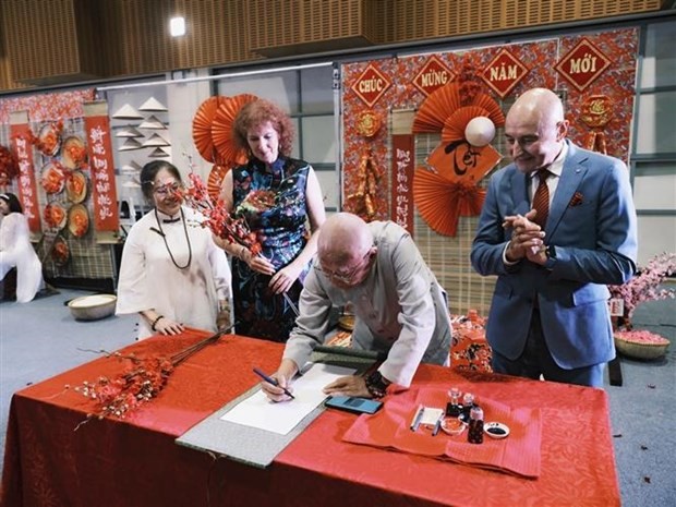 Le gouverneur du Territoire du Nord de l'Australie, Hugh Heggie (gilet bleu), observe la calligraphie lors de l'événement. Photo : VNA