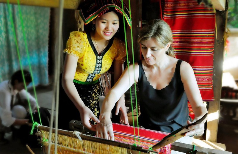 Une touristre étrangère découvre les étapes du tissage du brocart dans le village de Mên. Photo : hanoimoi.com.vn
