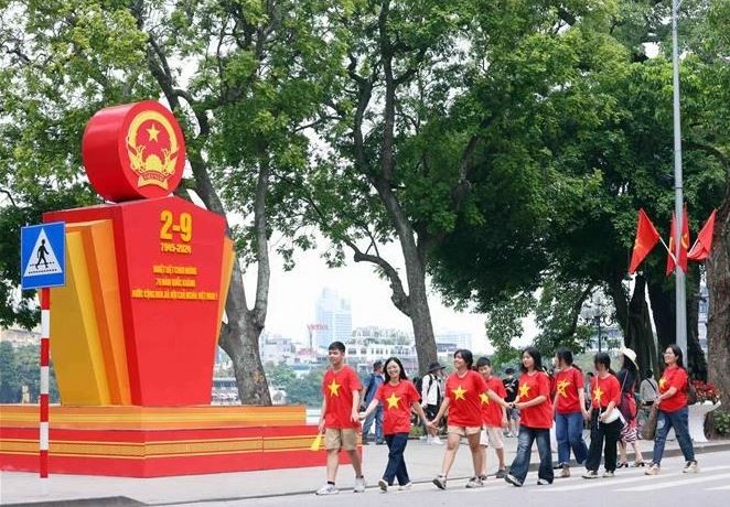 Des jeunes marchent en liesse devant un paneau célébrant la 79e Fête nationale du Vietnam, près du lac Hoàn Kiêm, à Hanoi. Photo : VNA.