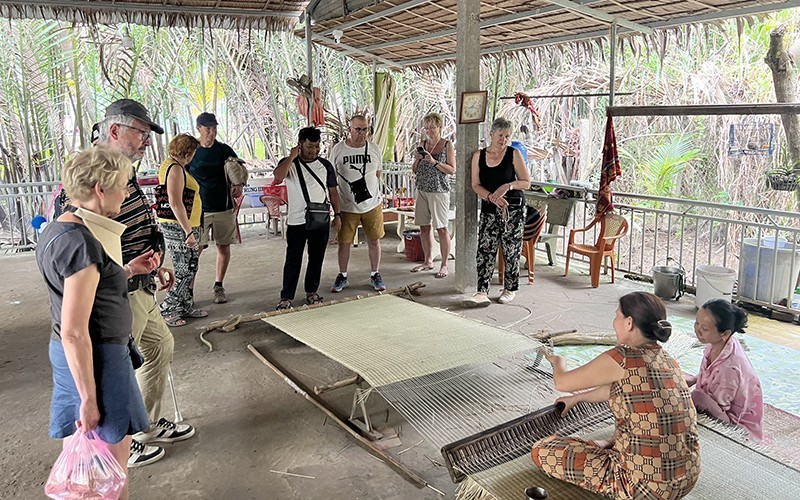 Des touristes étrangers regardent des villageois pratiquant le tissage des nattes dans la commune de Nhon Thach, province de Bên Tre. Photo : NDEL