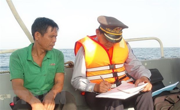 Un agent des forces de l'ordre de Quang Binh examine le journal de bord d'un bateau de pêche| Photo: AVI.