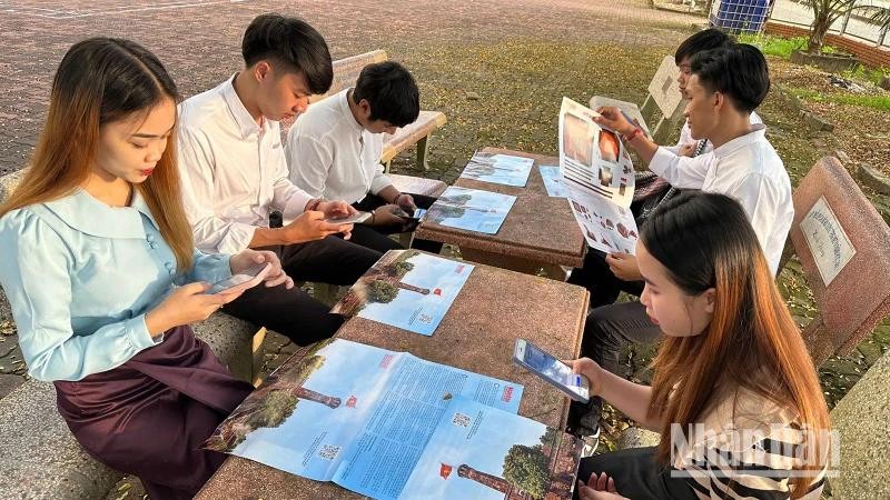 Des étudiants lao à Son La font l'expérience de la technologie numérique en scannant les codes QR pour en savoir plus sur le Jour de la libération de la capitale Hanoi dans la publication spéciale « la Tour du drapeau de Hanoi » du journal Nhân Dân. Photo : NDEL.