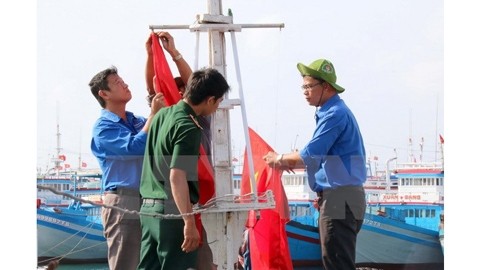 Les jeunes volontaires aident les pêcheurs à hisser les drapeaux sur le mât des navires. Photo: VNA.