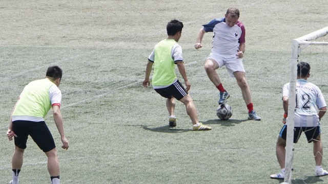 L’ambassadeur de France (maillot tricolore) joue au football.
